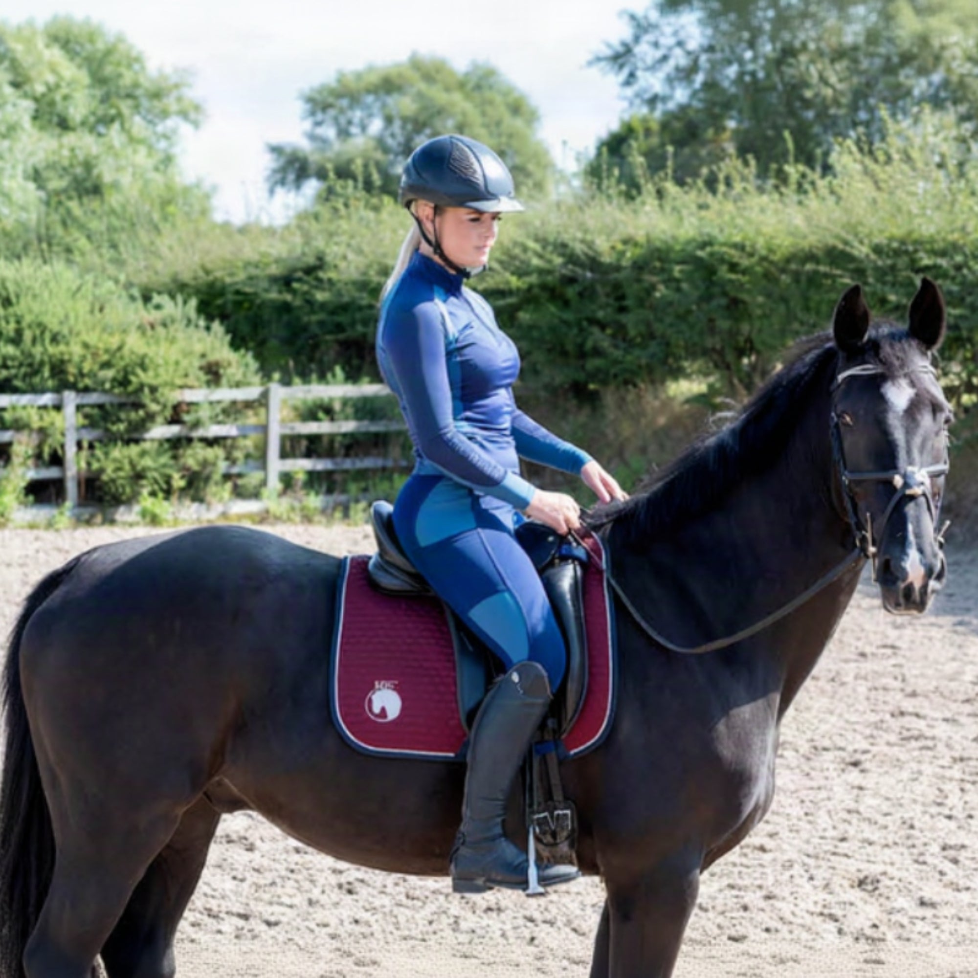 A woman wearing a blue and black horse riding base layer top, sitting on a horse.