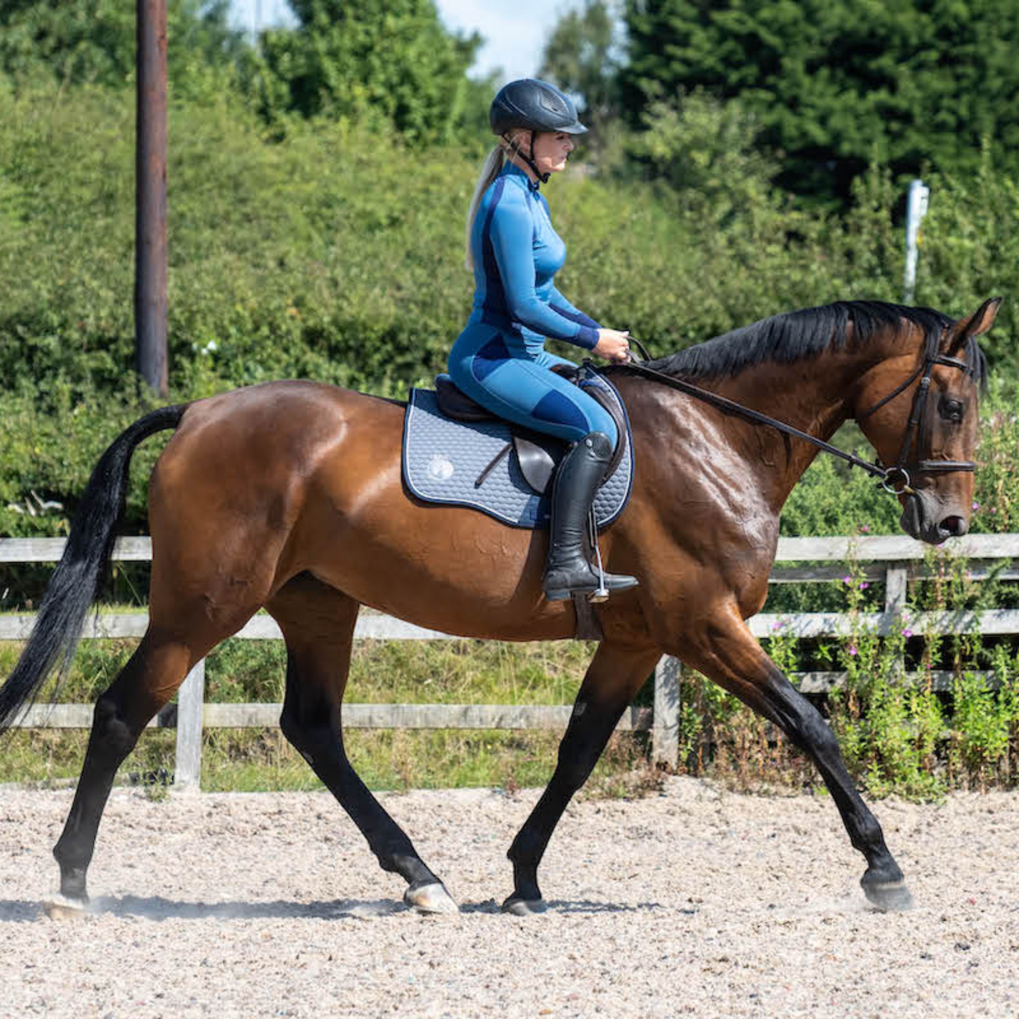 A horse wearing a grey saddle pad with a high wither cut, galloping in an outdoor arena.