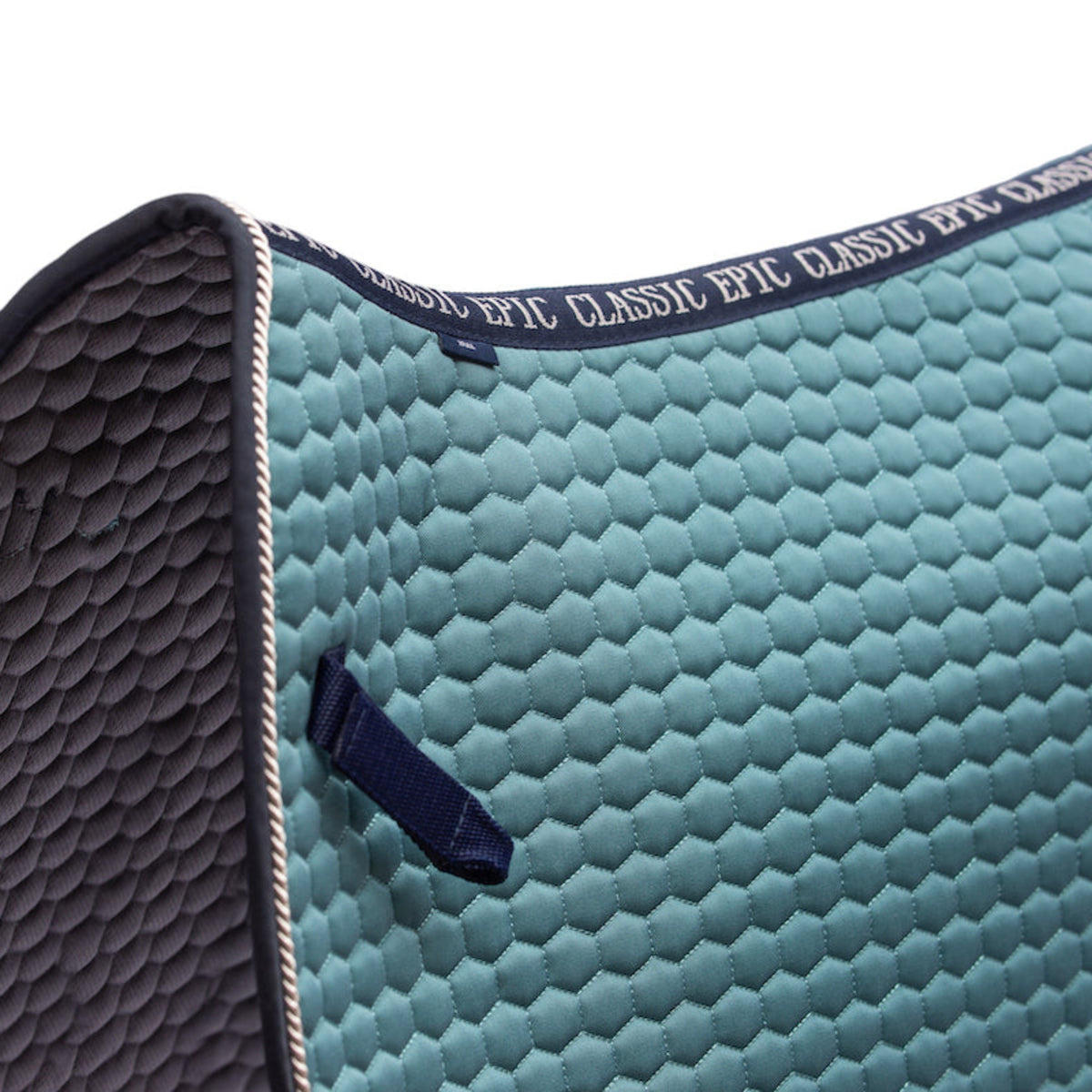 Close-up of a quilted equestrian saddle pad in a muted teal-green color with a dark navy trim and a matching pull tab, featuring the text 'EPIC CLASSIC EPIC' on the strap.