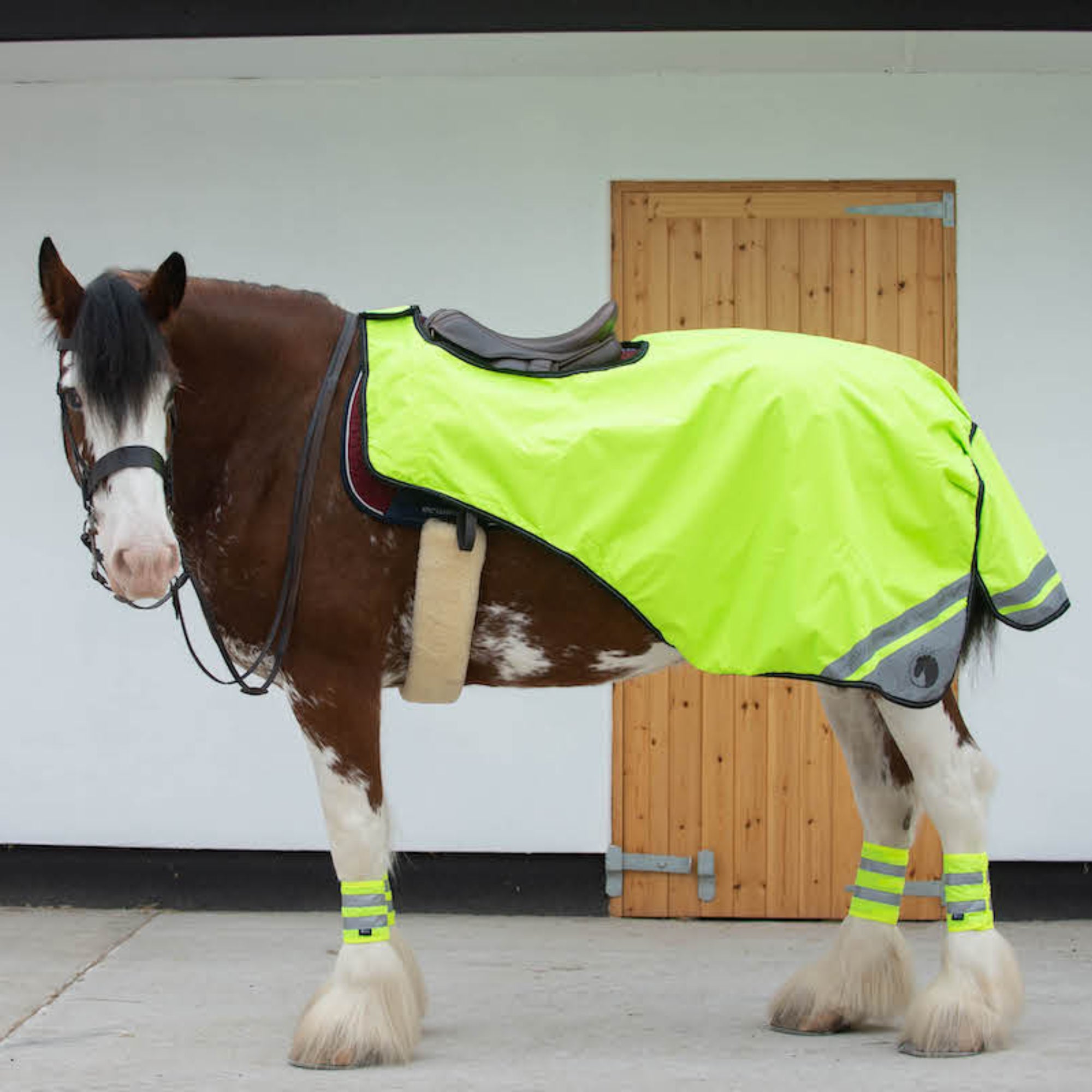 A horse wearing a yellow waterproof exercise sheet that is fluorescent, standing in front of stable doors.